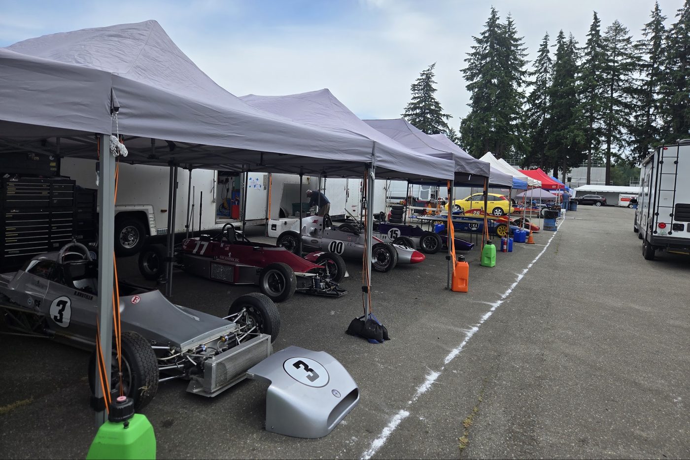 A row of vintage Formula Fords under paddock tents, the number 3 car in front with its nose off
