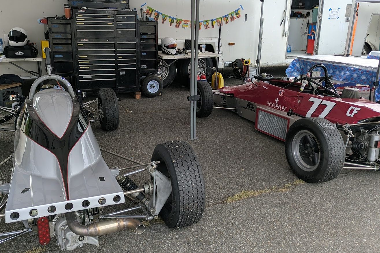 The tail of the number 3 car beside a red number 77 under a paddock tent